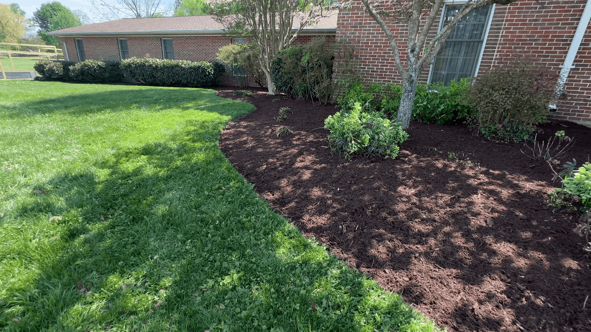 Village Baptist Church, with a large, freshly mulched garden bed bordered by green grass and various shrubs and small trees.